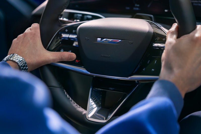 Close-up of a Man About to Press the V-Button on the 2026 OPTIQ-V Steering Wheel | Ingersoll Cadillac of Danbury in Danbury CT