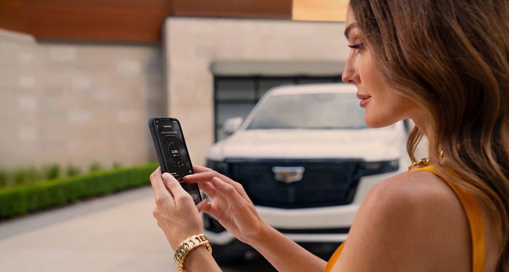 lady checking her mobile with a Cadillac vehicle background | Ingersoll Cadillac of Danbury in Danbury CT